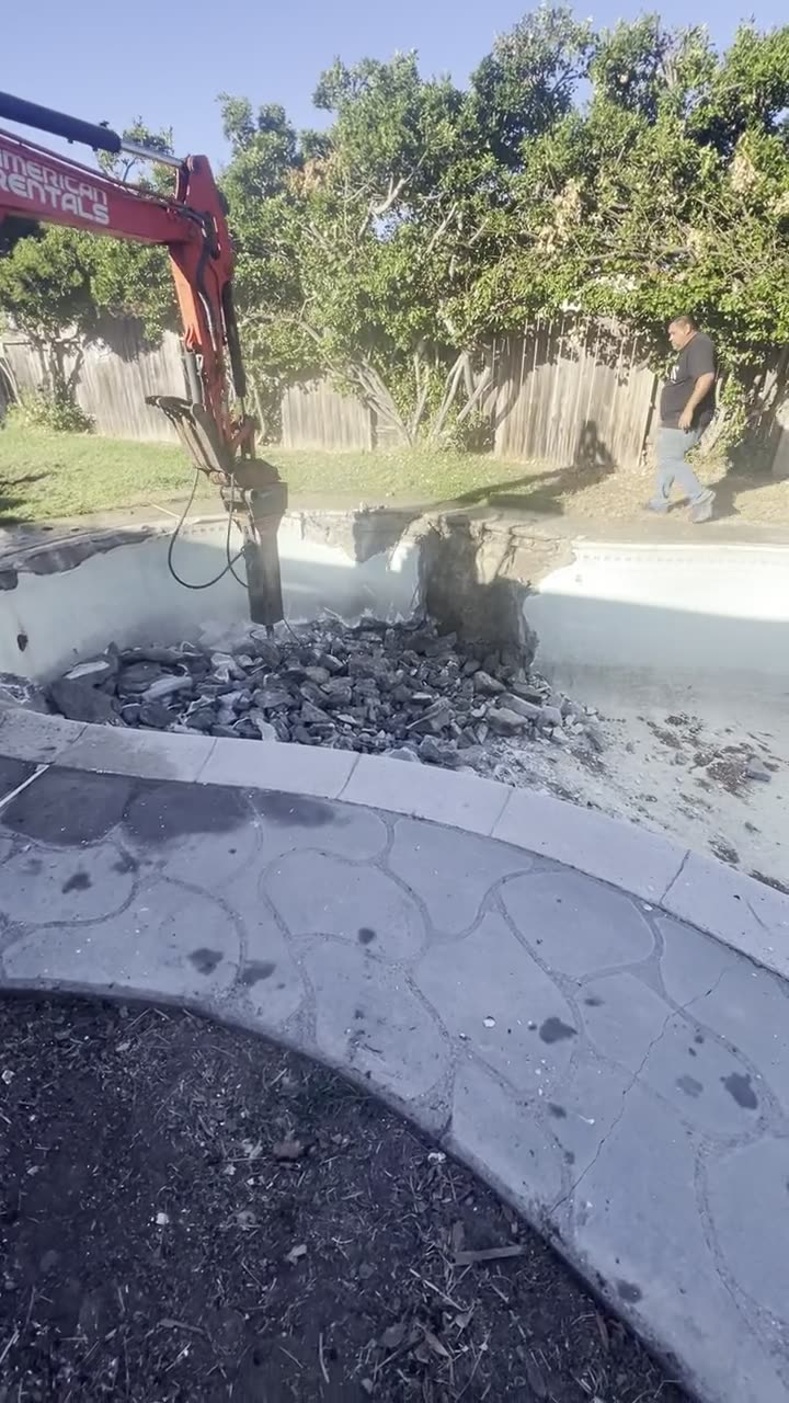 Excavator breaking up a swimming pool during demolition