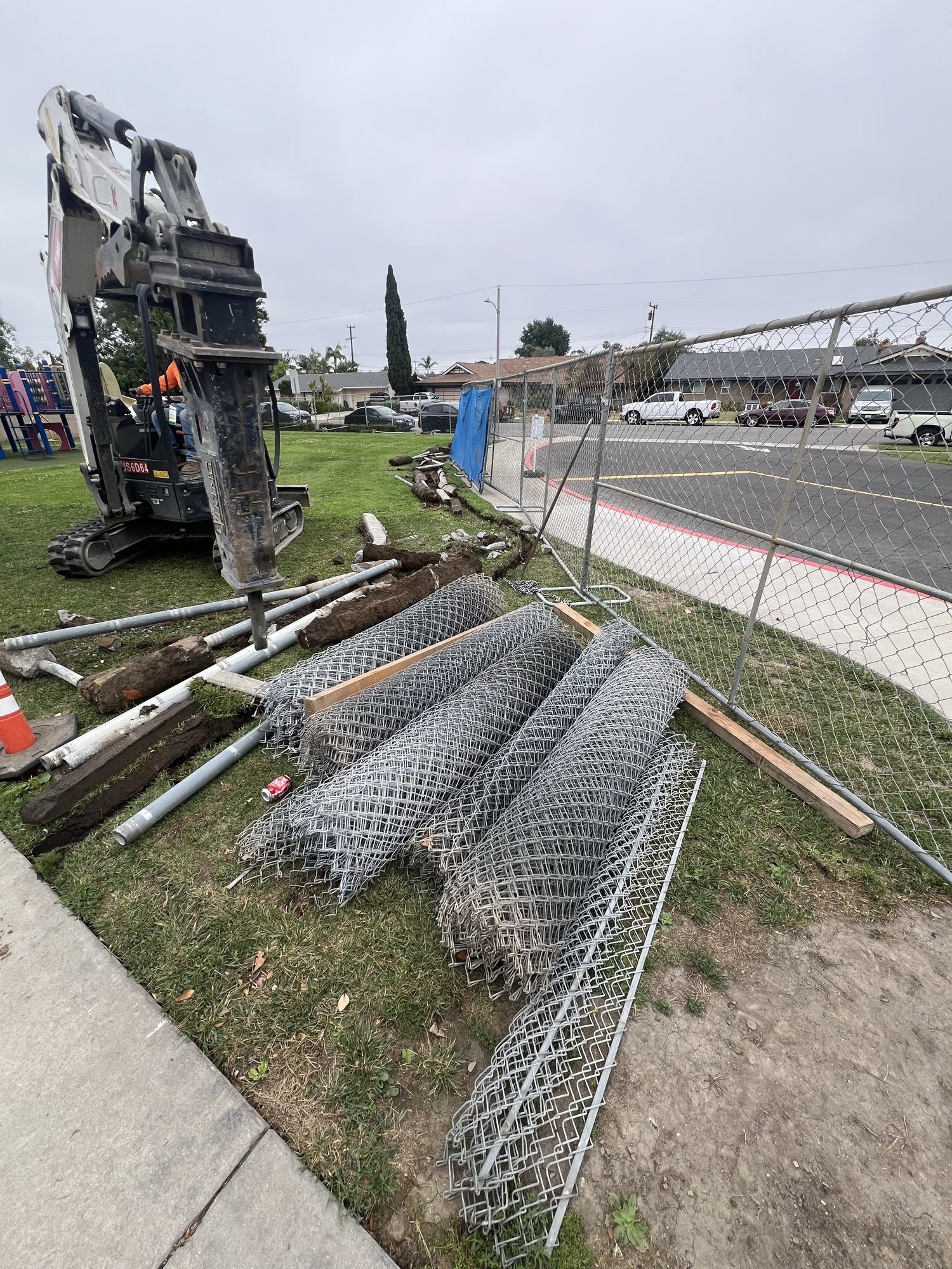 Excavator removing chain link fencing during demo
